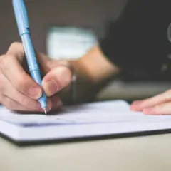 Dłoń pisząca niebieskim długopisem w notatniku.
