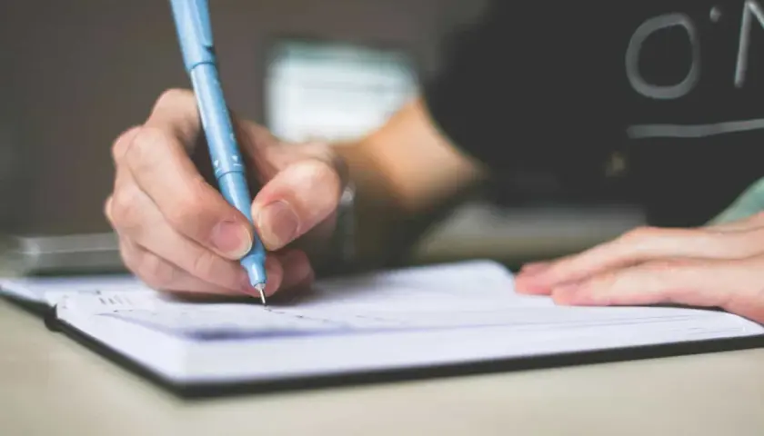 Dłoń pisząca niebieskim długopisem w notatniku.