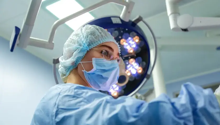Chirurg w masce i czepku na tle lampy operacyjnej.